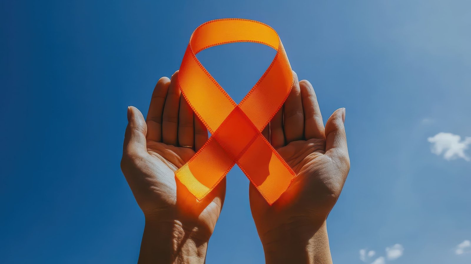 Hands holding an orange awareness ribbon against a blue sky