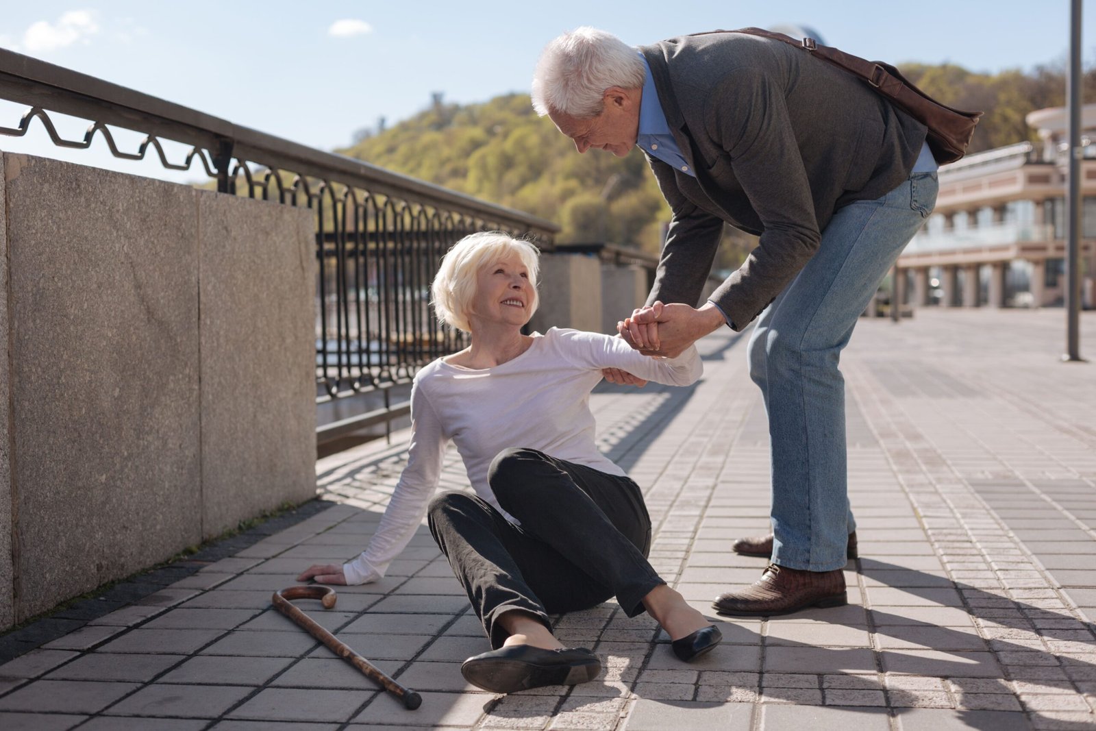 Man helping an older woman who has fallen on a walkway