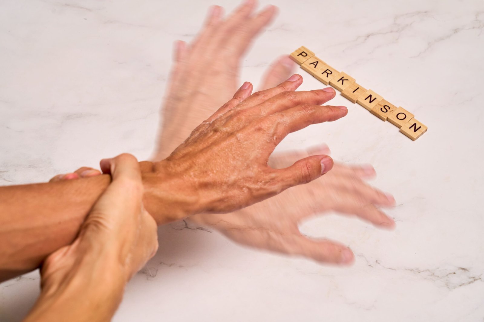 Trembling hands next to letter tiles spelling Parkinson